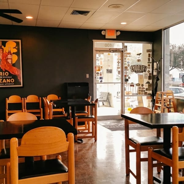 Interior of a restaurant with dark walls, wooden tables and chairs, and large windows.