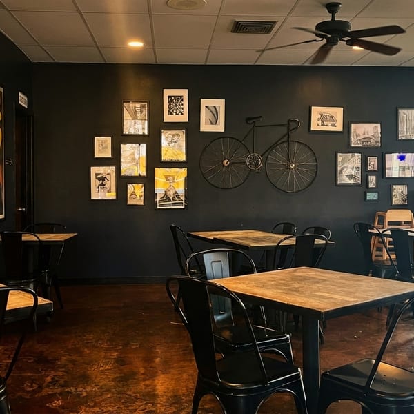 A restaurant dining room with dark walls, wooden tables, black chairs, and eclectic wall art.