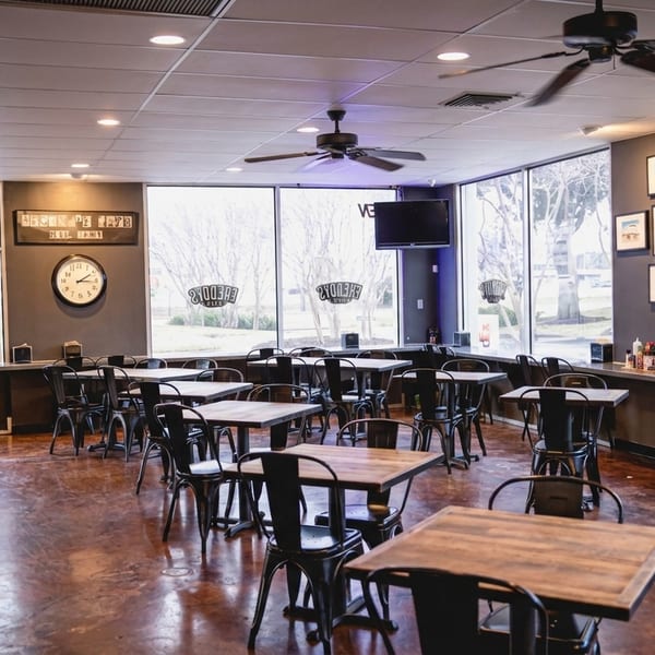 Empty dining room at Freddy's Cafe with dark tables and chairs, large windows, and ceiling fans.
