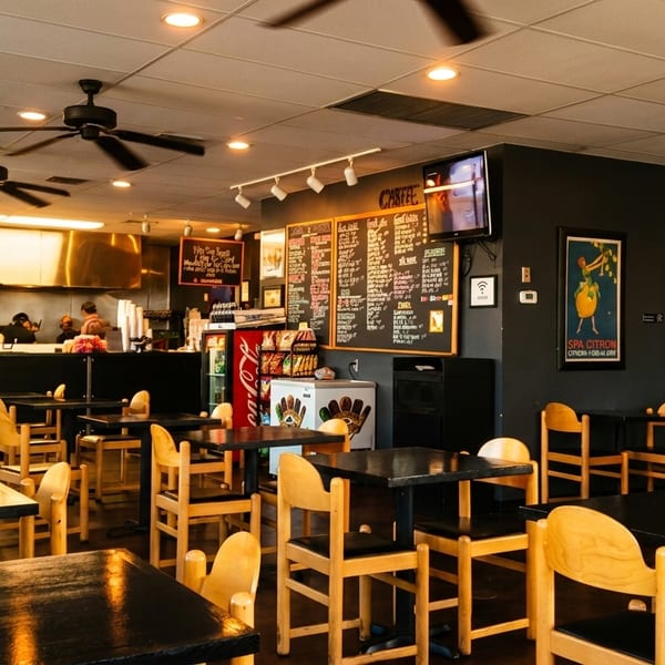 Interior of a casual restaurant with dark tables, wooden chairs, and a counter with staff.